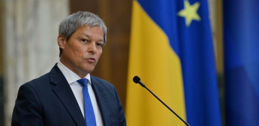 dacian ciolos intr-o declaratie de presa cu drapelul romaniei si al ue in spate